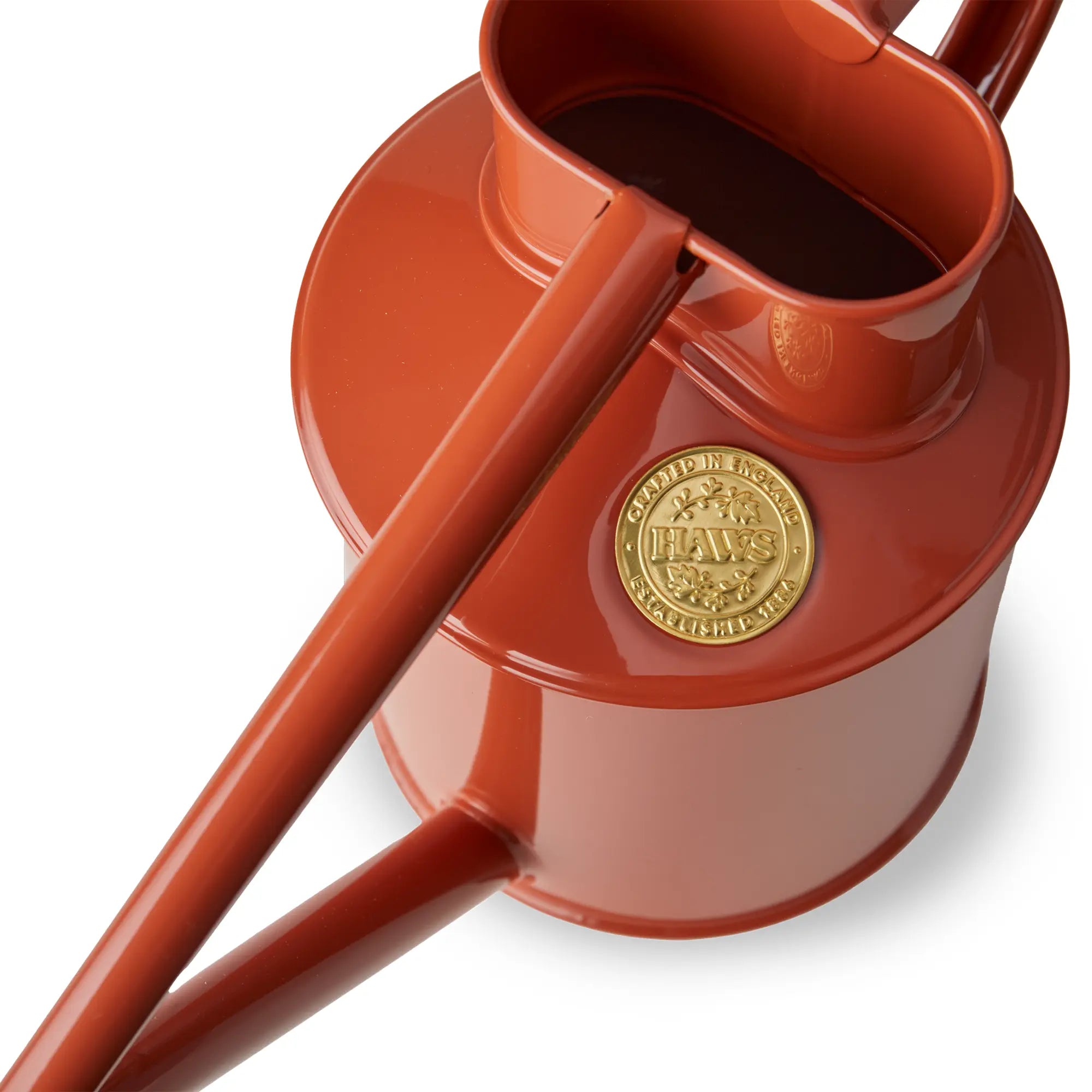 A close-up view of the top of a Haws terracotta-coloured Fazeley Flow metal watering can, showing the detail of the Haws embossed badge.