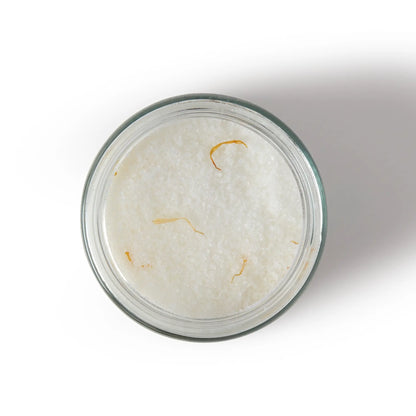 View from above of glass jar of white Homework bath salts with orange pieces on a white background.