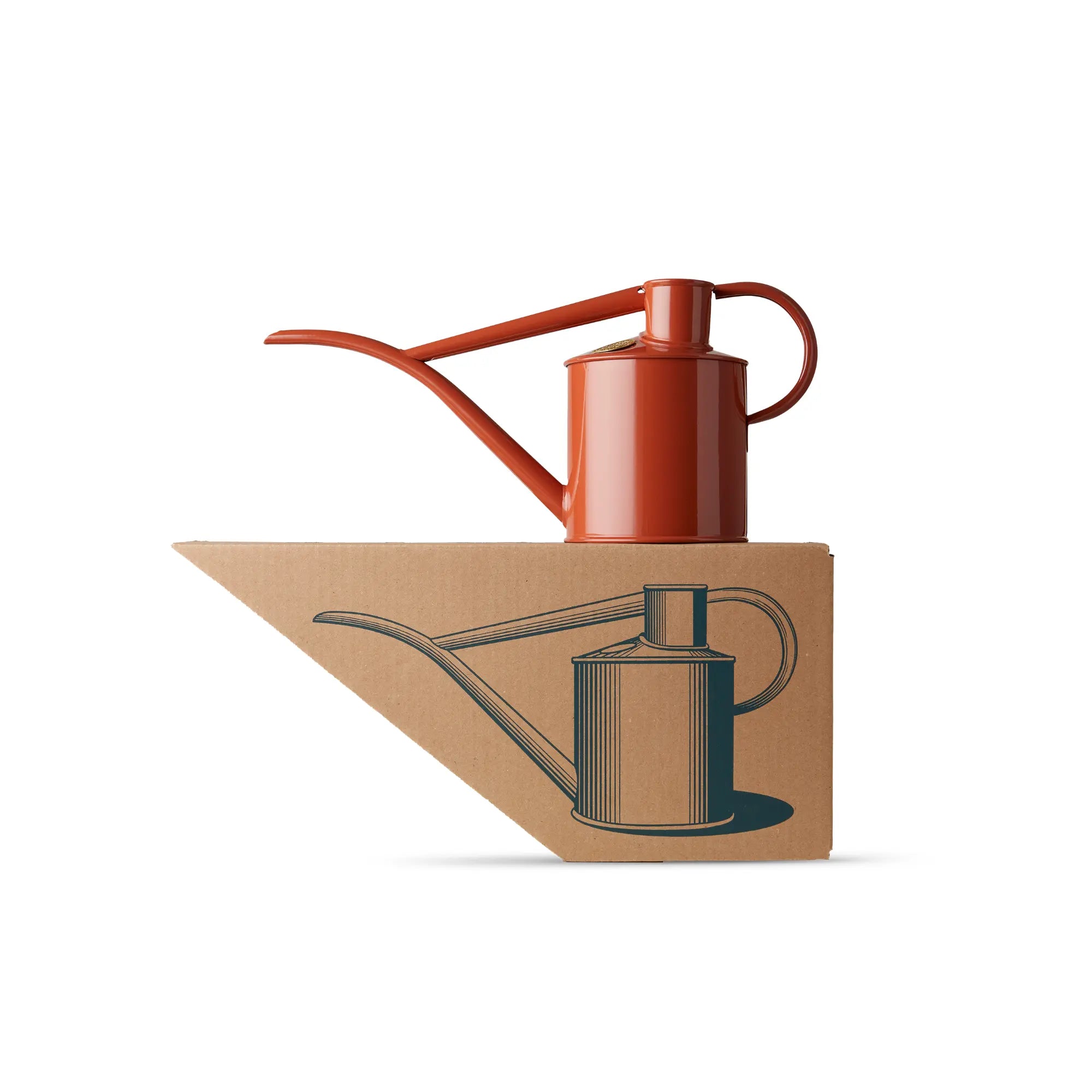 A terracotta-coloured Haws Fazeley Flow metal watering can on top of its packaging - a shaped cardboard box with a picture of the watering can.