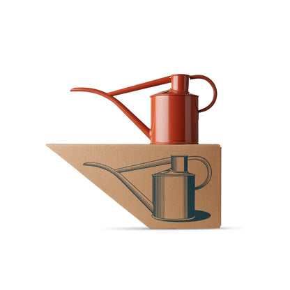 A terracotta-coloured Haws Fazeley Flow metal watering can on top of its packaging - a shaped cardboard box with a picture of the watering can.