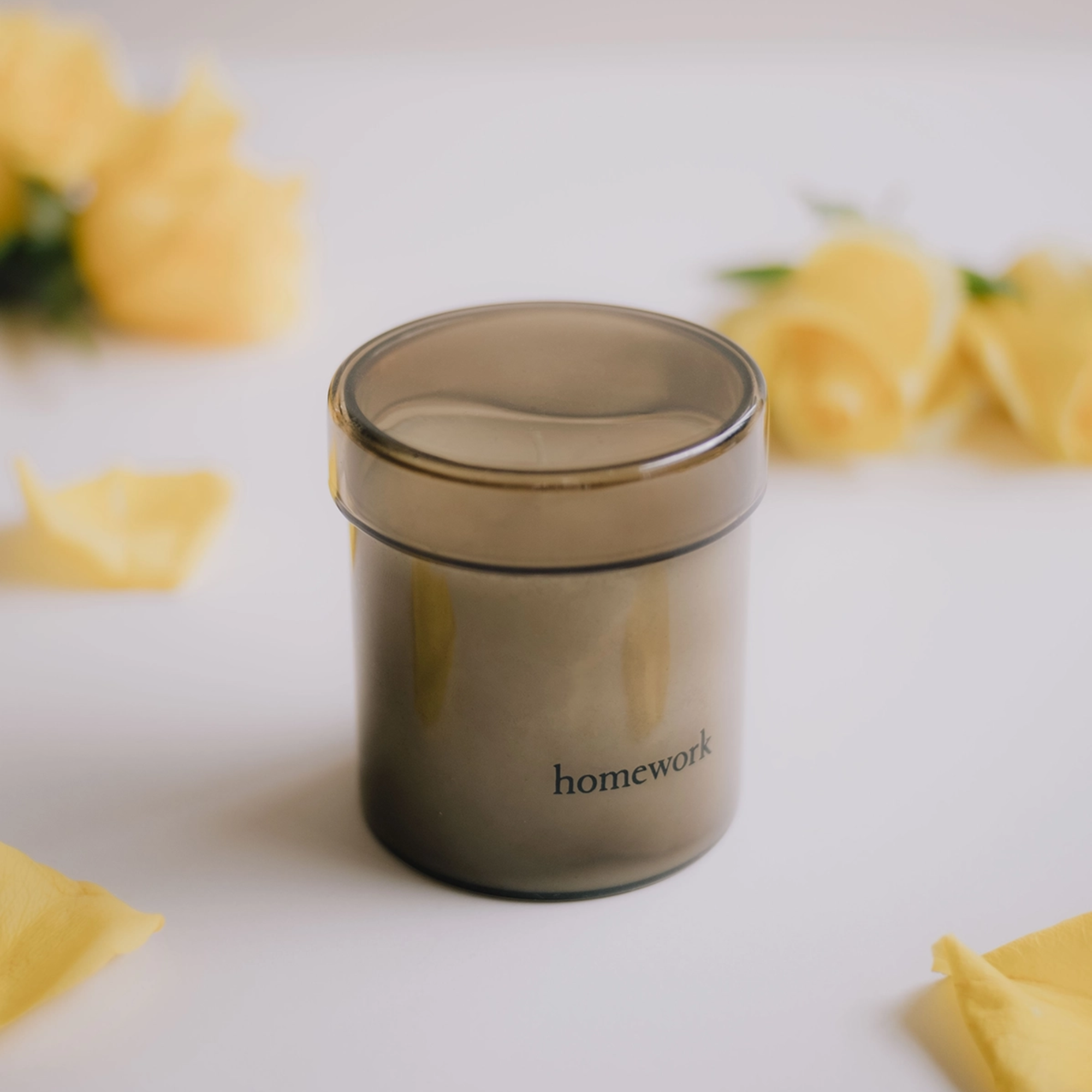Glass jar candle with lid labeled 'Homework' with yellow flowers in the background